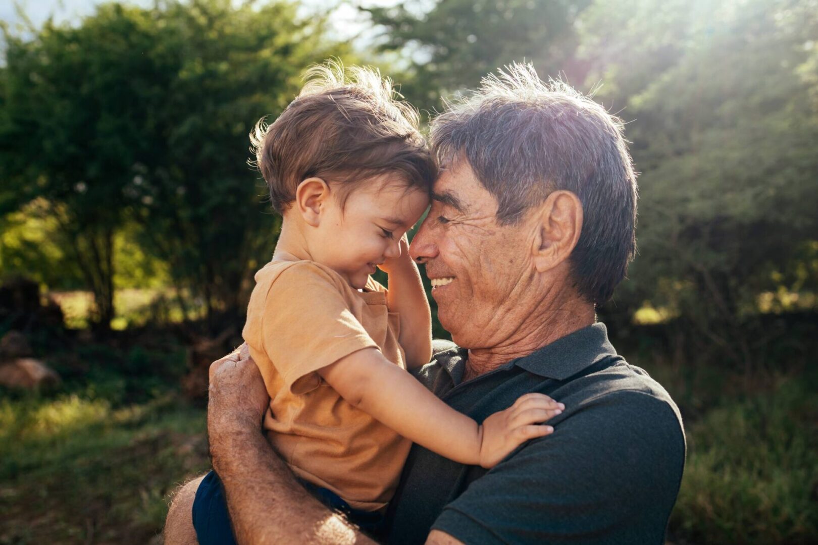 Grandfather joyfully holds his smiling young granddaughter outdoors.