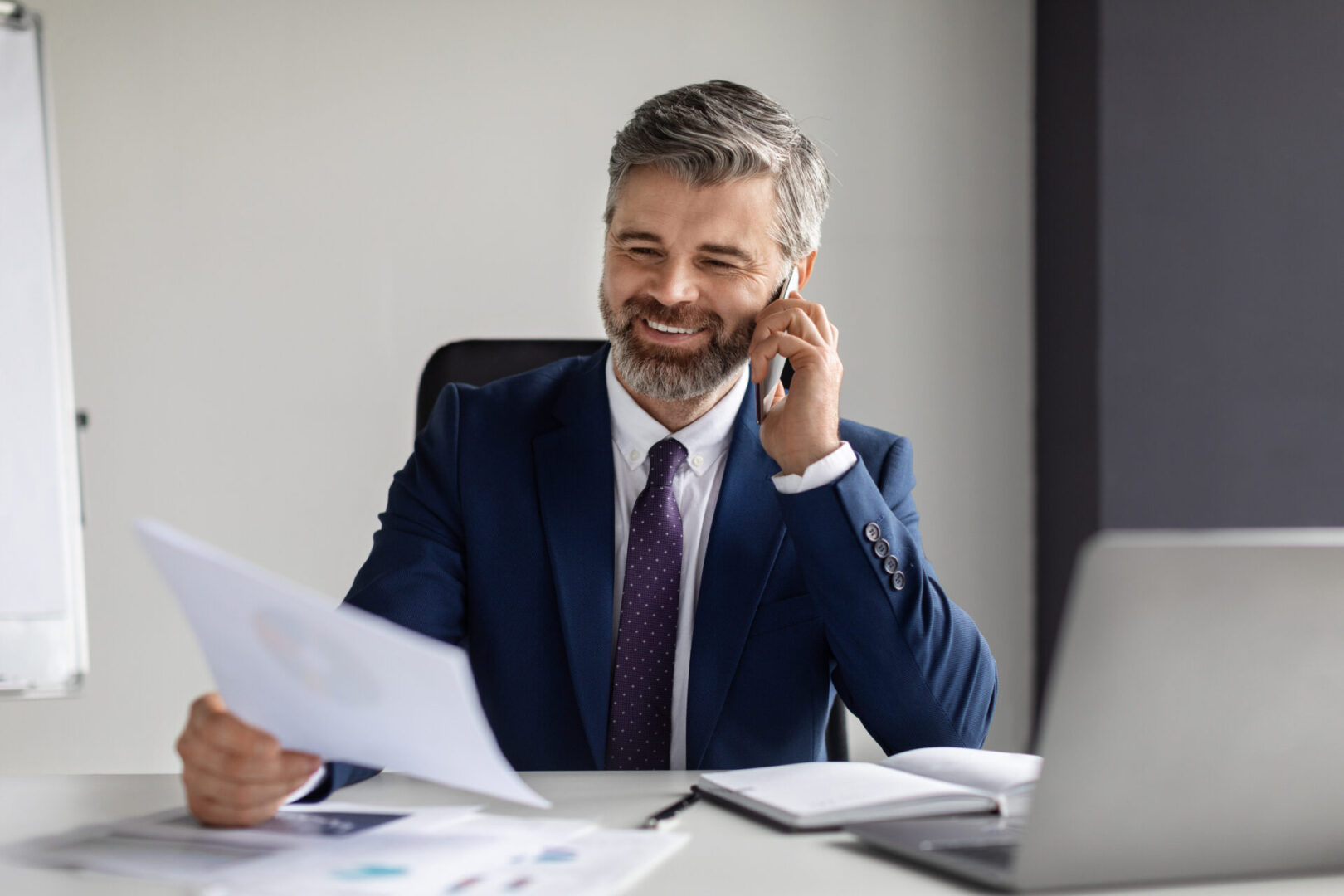 Smiling businessman talking on phone while reviewing documents.