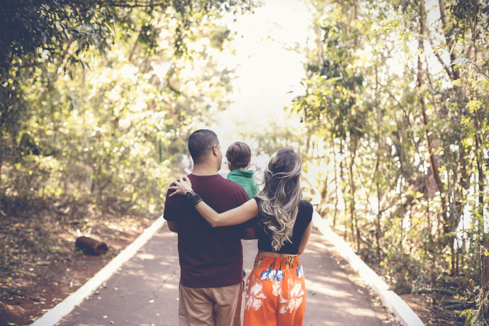 A family walk on a sunlit forest path with arms around each other.