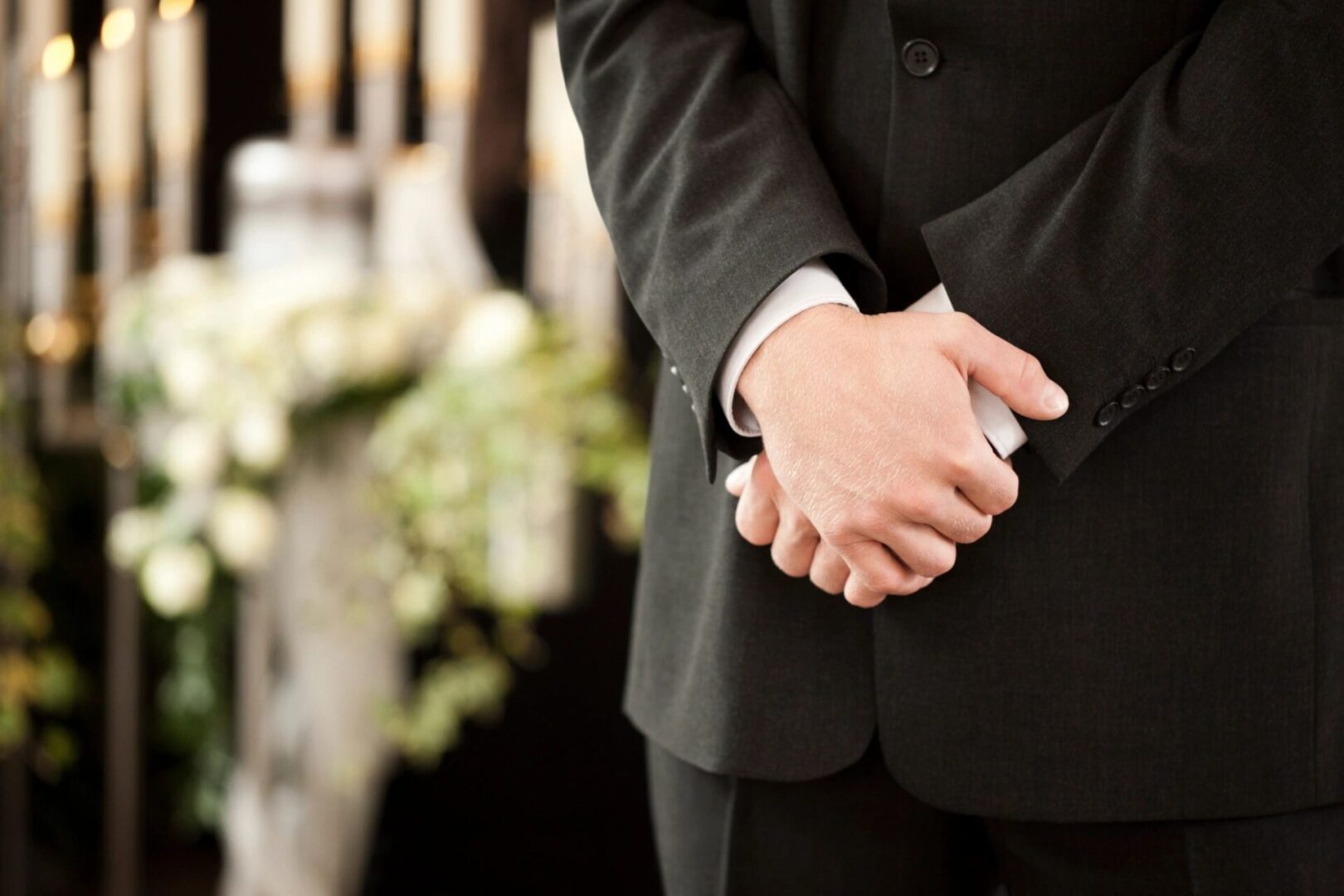 Person in a suit standing with hands clasped at a formal event.